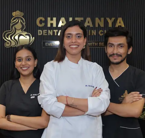 Three staff members in clinical coats standing together in front of the clinic's branded wall sign.