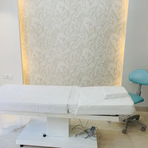 An empty treatment bed with fresh linens beside a teal stool and a skin treatment device.